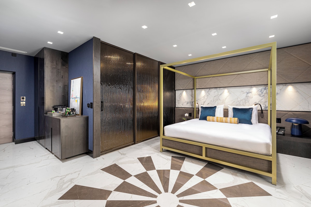 A modern bedroom with a four-poster bed, a desk, and a wardrobe.