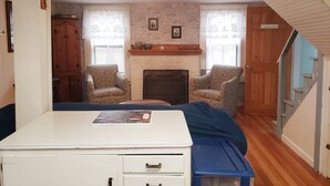 A room with a white desk, two patterned armchairs, a fireplace, and a staircase.
