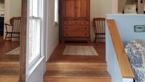 A hallway with wooden flooring, a wooden cabinet, and a mirror on the left.