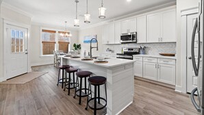A modern kitchen with white cabinetry, a large island with stools, stainless steel appliances, and pendant lighting. - Serenity Tides PCB- Golf Cart, Games, MiniGolf & Dogs OK – 3 Blocks to Beach (Panama City Beach)