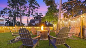 A backyard with a fire pit, two Adirondack chairs, and a string of lights. - Serenity Tides PCB- Golf Cart, Games, MiniGolf & Dogs OK – 3 Blocks to Beach (Panama City Beach)