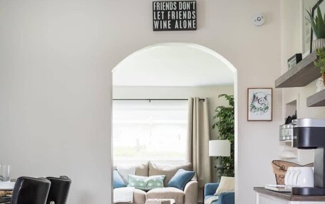 A modern kitchen with a dining area, a coffee machine, and a sign that reads "FRIENDS DON'T LET FRIENDS WINE ALONE."