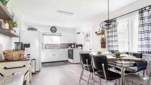 A modern kitchen with white cabinets, a dining area with a round table and chairs, and a hanging light fixture. - Cedar Creek Cottage-Idyllic Setting & Dog Friendly (Cedar)