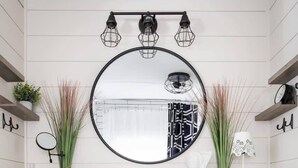 A white vanity with a round mirror, blue doors, and a shelf with toiletries. - Cedar Creek Cottage-Idyllic Setting & Dog Friendly (Cedar)