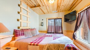 A cozy bedroom with a wooden ceiling, a bed with a quilt, a TV, and a window with curtains. - Walk to Lake Cabin great for kids &  Pets Spa BBQ WiFi King Bed Ski Free Coffee (Big Bear Lake)