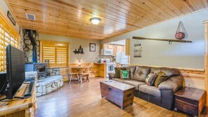 A cozy cabin interior with a stone fireplace, wooden furniture, and a kitchen area. - Walk to Lake Cabin great for kids &  Pets Spa BBQ WiFi King Bed Ski Free Coffee (Big Bear Lake)