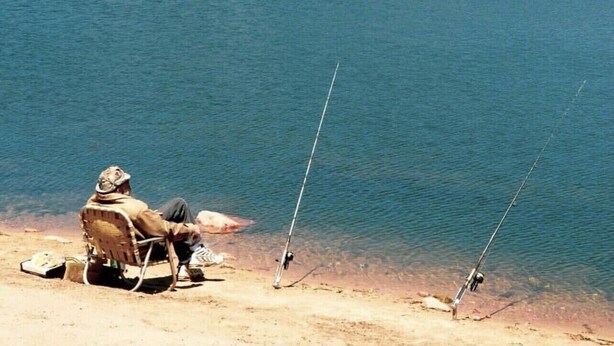 A lakeside scene with a person fishing, clear water, and a forested hill in the background. - Walk to Lake Cabin great for kids &  Pets Spa BBQ WiFi King Bed Ski Free Coffee (Big Bear Lake)