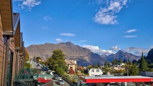 Une ville avec une chaîne de montagnes en arrière-plan, une route bordée de voitures garées et une station-service bien visible.