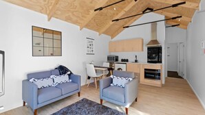Un salon moderne avec un plafond haut, une cuisine dotée de meubles en bois et un coin repas avec une table et des chaises.