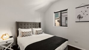 Une chambre à coucher comprenant un lit, une table de chevet, une fenêtre et une œuvre d’art accrochée au mur.