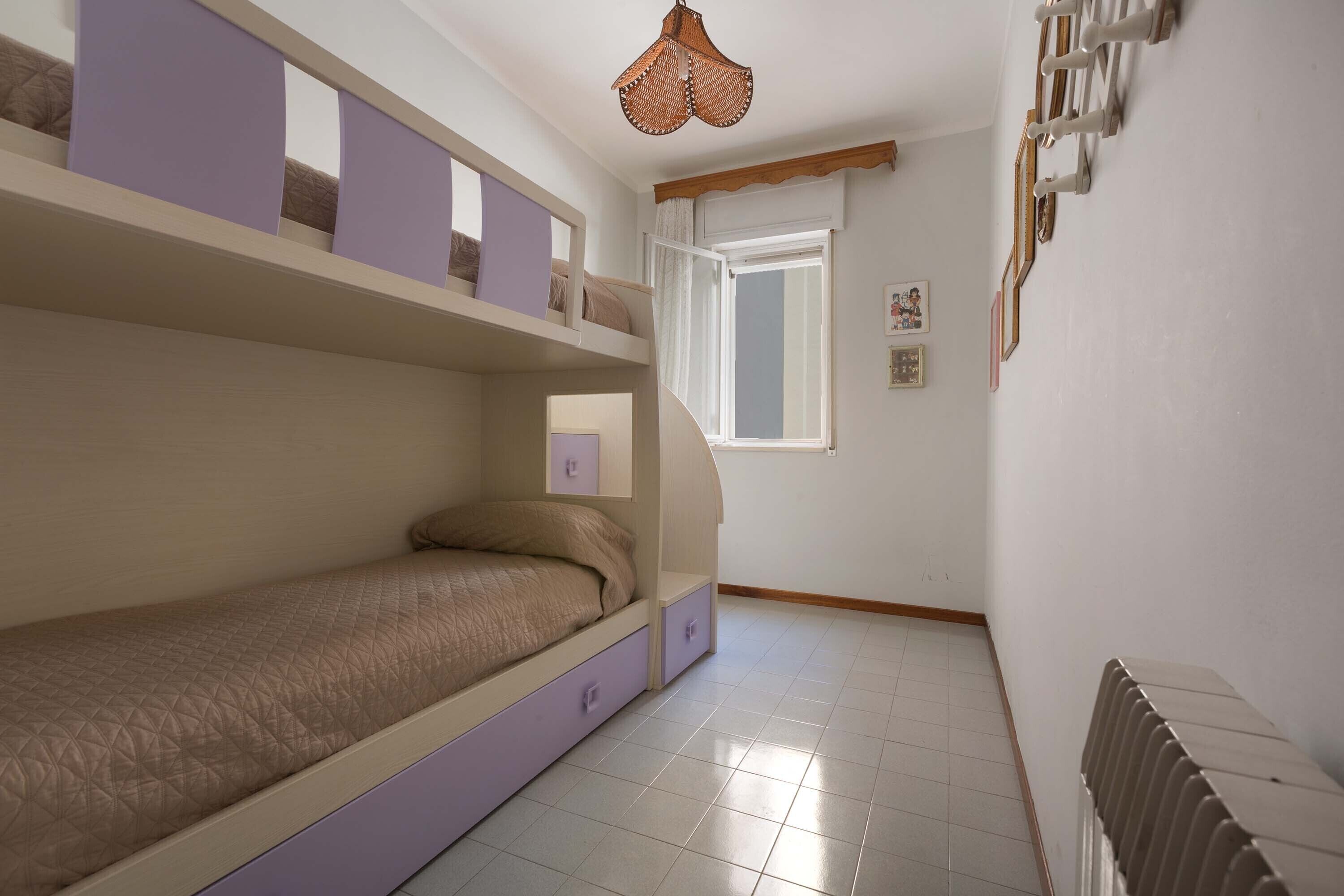 Une chambre avec des lits superposés, une fenêtre avec des rideaux, un radiateur et des tableaux accrochés au mur.