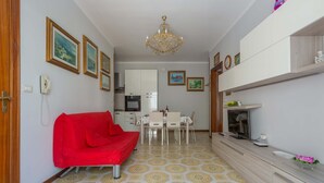Een kleine leefruimte met een kitchenette, een eethoek en een rode bank.