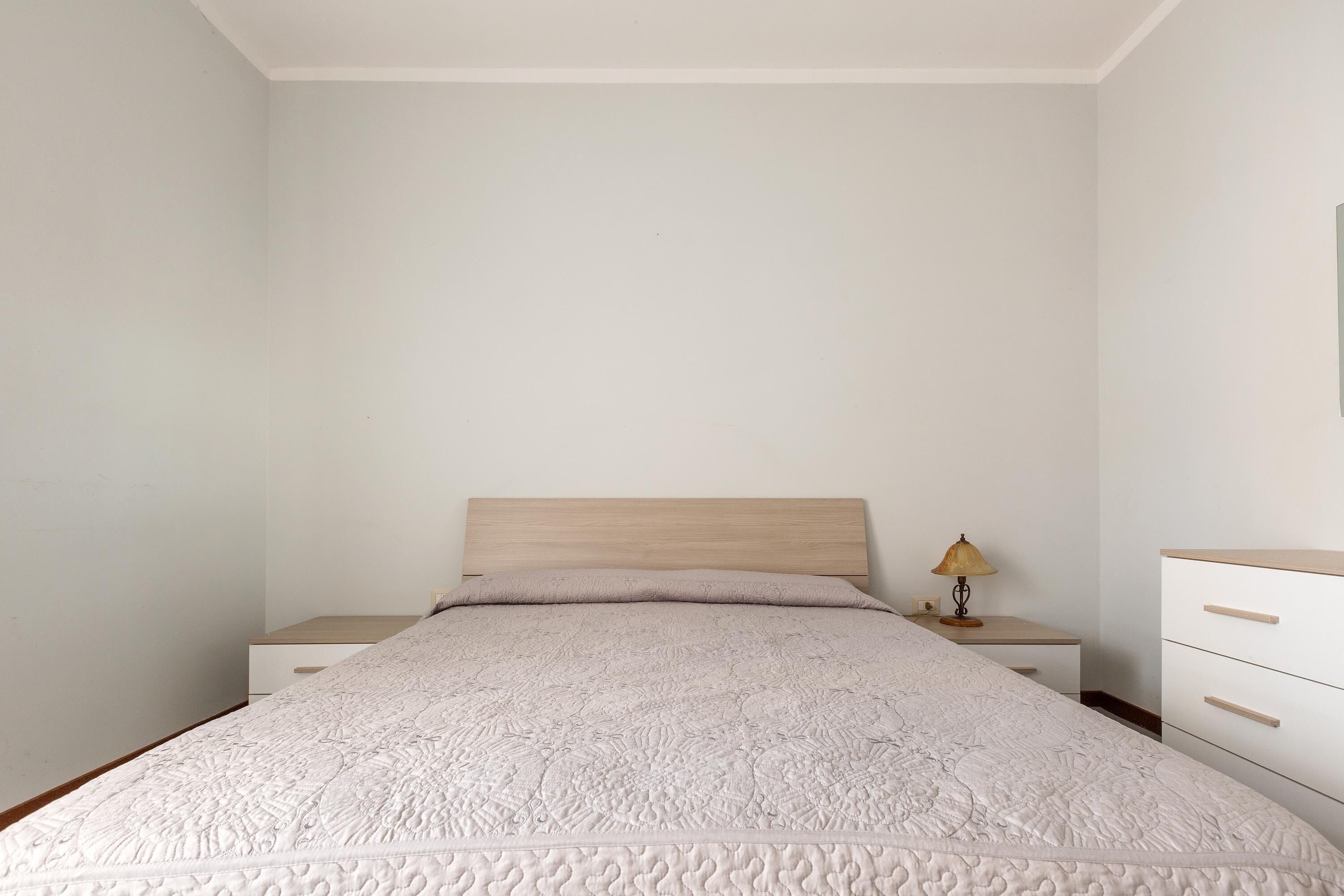 A bedroom with a bed, a nightstand, a lamp, and a dresser.
