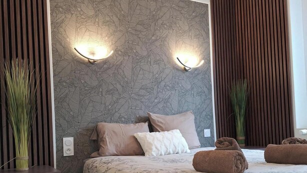 A modern bedroom with a large bed, two wall-mounted lights, and a decorative wall panel.