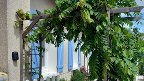 A stone pathway leading to a white wooden gate, with a pergola covered in green foliage.