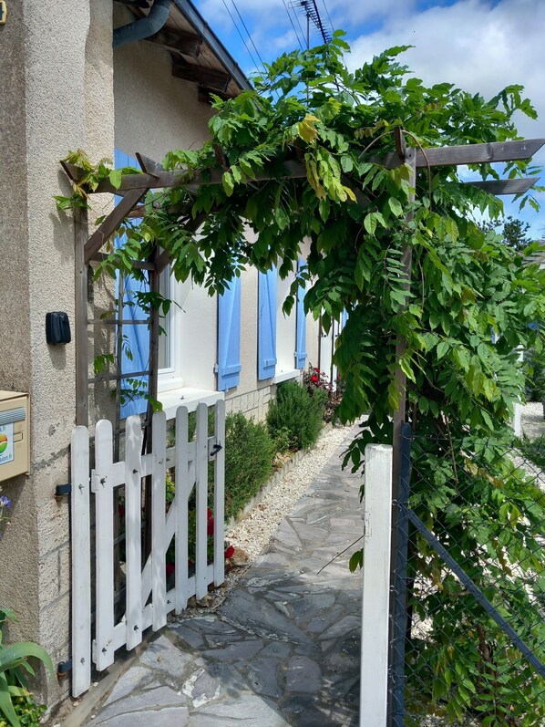 A stone pathway leading to a white wooden gate, with a pergola covered in green foliage. - Gîte du Canal de Berry II (Selles-sur-Cher)