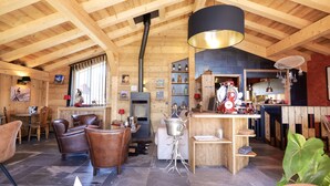 A rustic wooden interior with a high ceiling, a fireplace, leather chairs, a bar area, and a variety of decorative items.