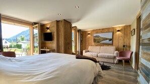 A hotel room with a large bed, a sofa, a chair, a TV, and a painting on the wall.