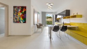 Uma cozinha moderna com armários amarelos, uma área de jantar com cadeiras e um quadro abstrato colorido na parede.