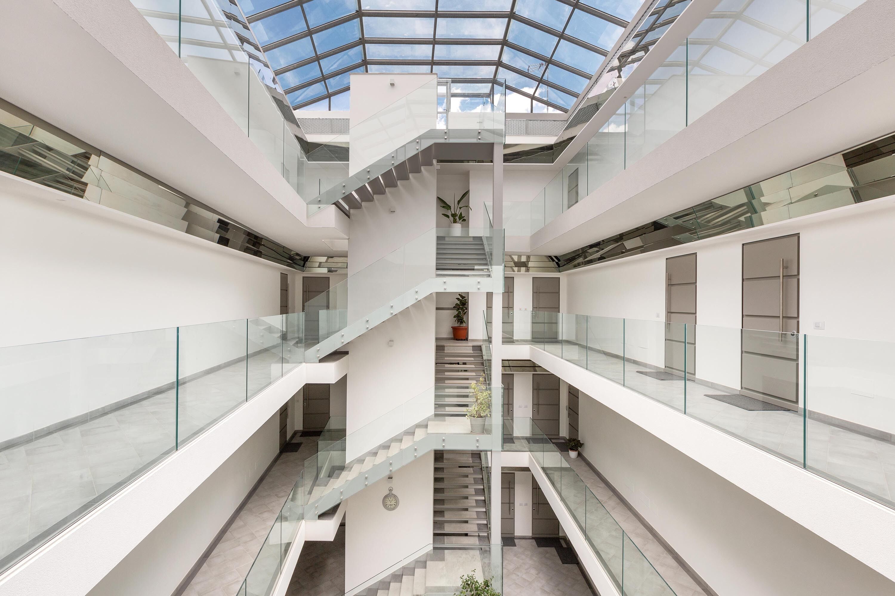 Un atrium à plusieurs niveaux, doté de rampes en verre et d’un escalier central.