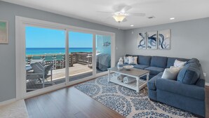 Un salon avec vue sur l’océan, un ventilateur de plafond et un canapé bleu.