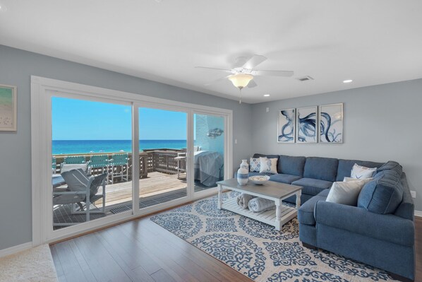A living room with a view of the ocean, a ceiling fan, and a blue couch.