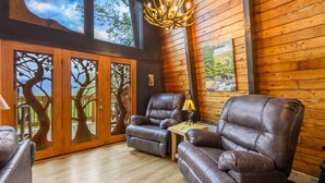 A wooden interior with two leather recliners, a small table with a lamp, and a door with tree cutouts. - Stunning view, location & Cabin amenities- 2.3 mi to Gatlinburg (Gatlinburg)
