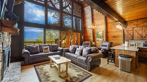 A cozy cabin interior with a fireplace, leather sofas, a dining area, and large windows offering scenic views. - Stunning view, location & Cabin amenities- 2.3 mi to Gatlinburg (Gatlinburg)