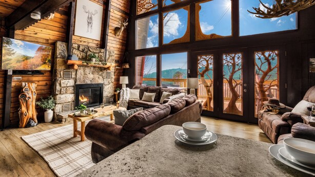 A cozy cabin interior with a stone fireplace, large windows, and a comfortable seating area. - Stunning view, location & Cabin amenities- 2.3 mi to Gatlinburg (Gatlinburg)
