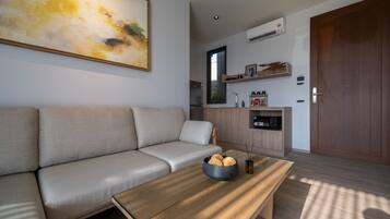 A modern living room with a sofa, a coffee table with decorative items, a kitchen area with a refrigerator, and a wooden door.