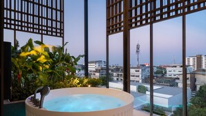 Uma banheira de hidromassagem com iluminação azul, rodeada por teto de madeira e grandes janelas com vista para a cidade.