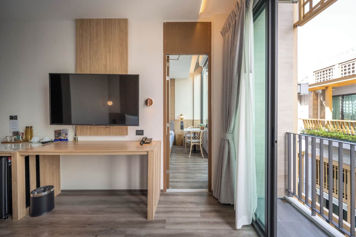 Ett modernt hotellrum med ett skrivbord i trä, en platt-TV, en papperskorg och en balkong med utsikt över byggnaden.