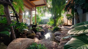 Um jardim interno tranquilo com fonte de água, pedras grandes e vegetação exuberante.