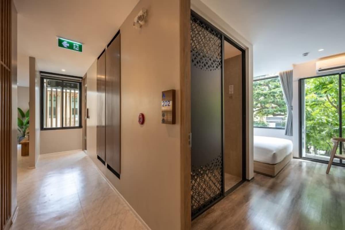 Corredor de hotel com uma cama, porta deslizante e vista para o verde lá fora.