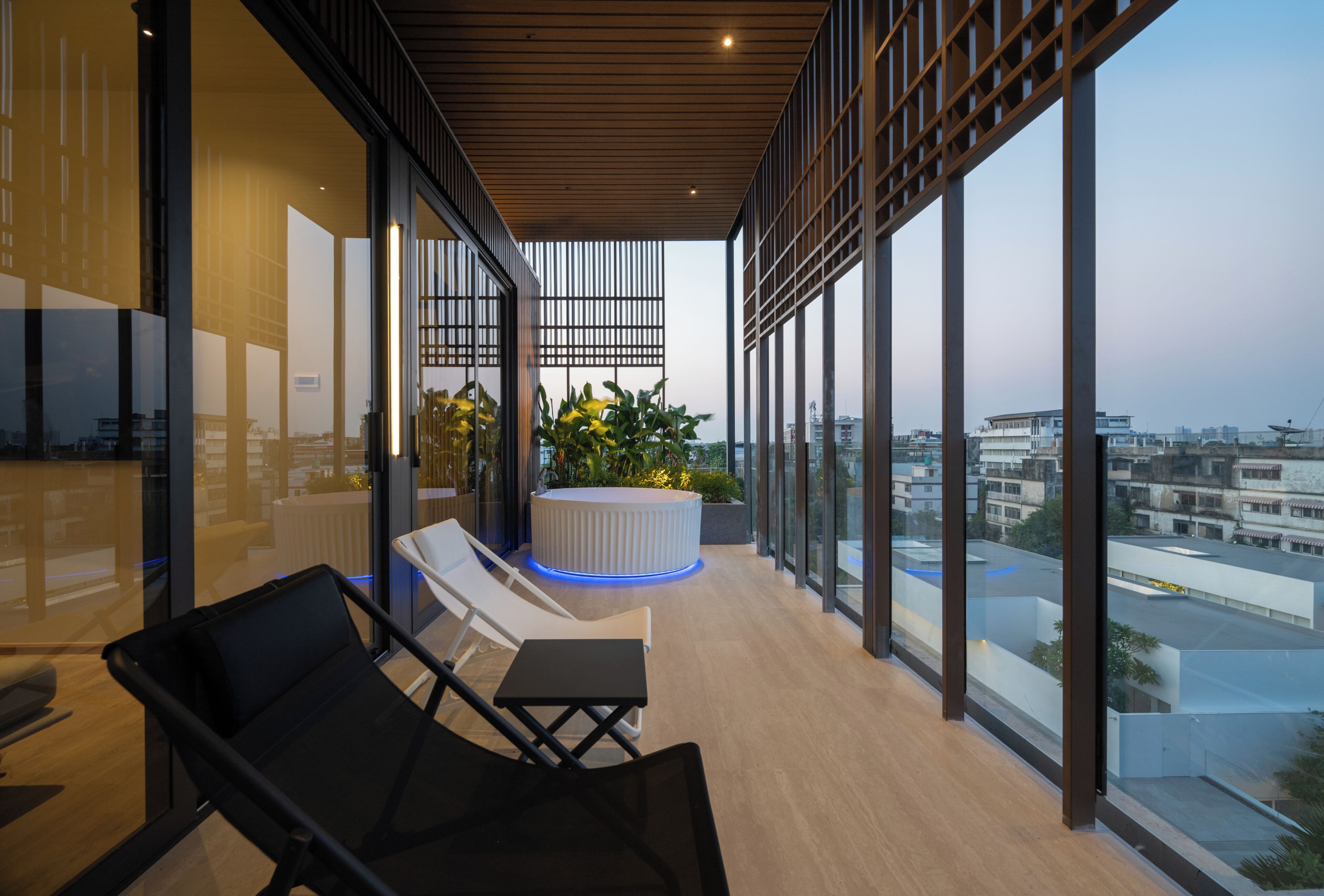 A modern balcony with lounge chairs, a round seating area, and large windows offering city views.
