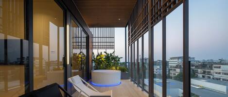 A modern balcony with lounge chairs, a round seating area, and large windows offering city views.
