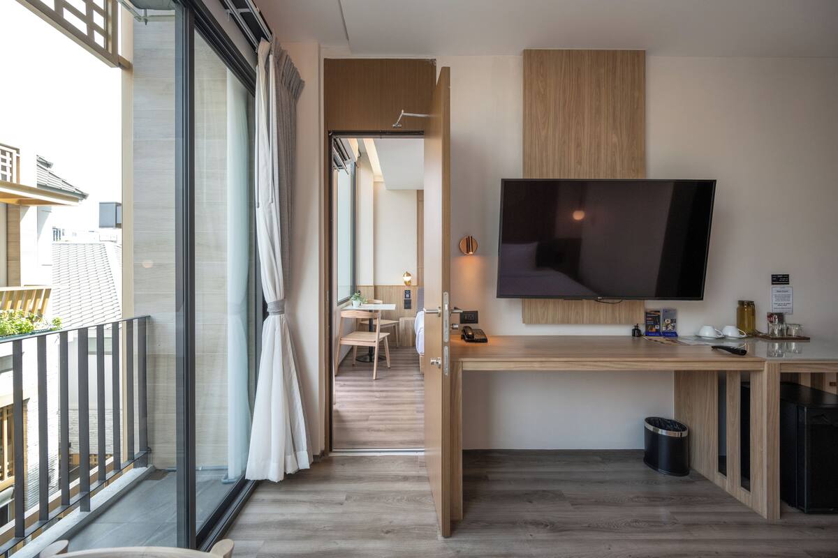 Ett modernt hotellrum med en stor TV, ett skrivbord i trä och en balkong med en glasdörr.