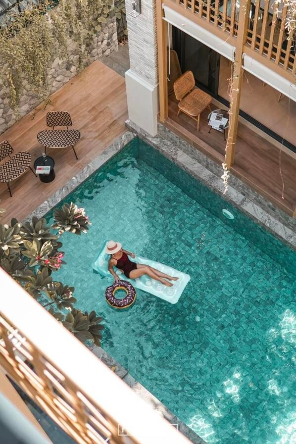 Relax by the pool surrounded by lush greenery and a wooden deck.
