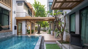 Uma área de piscina moderna ao ar livre, com pergolado, assentos e um pequeno jardim.