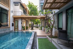 Relax by the rectangular pool surrounded by lush greenery and a shaded seating area.