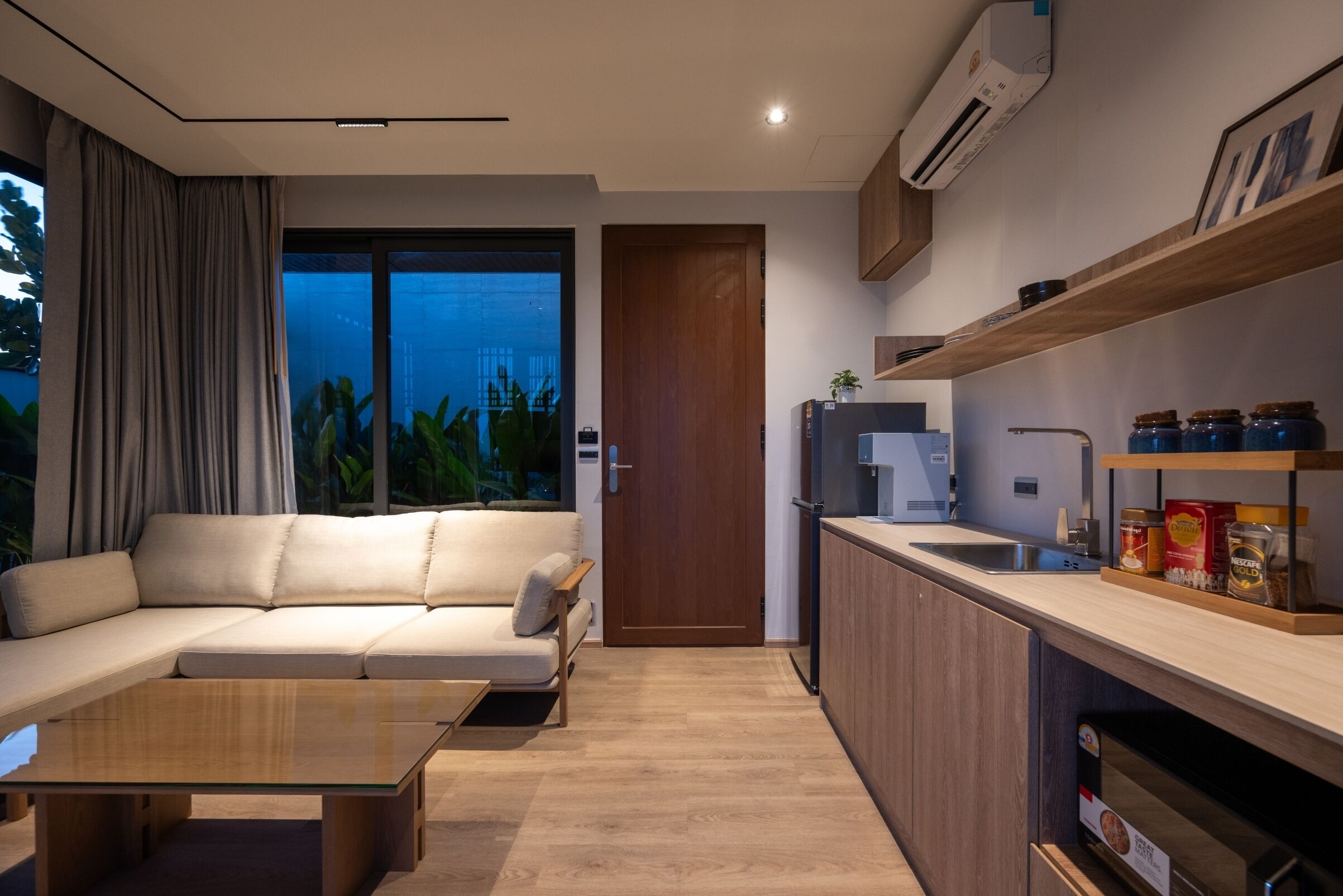 Een moderne woonkamer met een bank, salontafel en een keukenhoek met een spoelbak en kastjes.