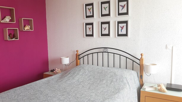 A bedroom with a bed, a nightstand, a lamp, and framed pictures on the wall.