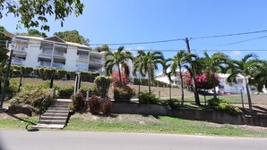A multi-story building with balconies, surrounded by palm trees and flowering plants. - Ocean view, 2-minute walk to the beach (Le Moule)