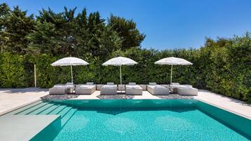 Una piscina con lettini e ombrelloni, circondata da un siepe.