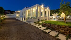 Une maison moderne avec une allée en gravier, un mur en pierre et un espace extérieur bien éclairé avec une piscine.
