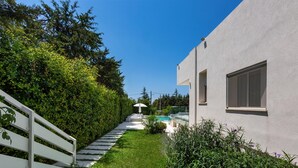 Une maison moderne à l’extérieur blanc, avec un escalier apparent menant à un espace extérieur couvert, et un jardin bien entretenu.