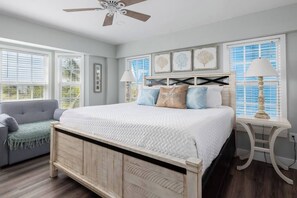A bedroom with a wooden bed, a gray sofa, and a white nightstand with a lamp.