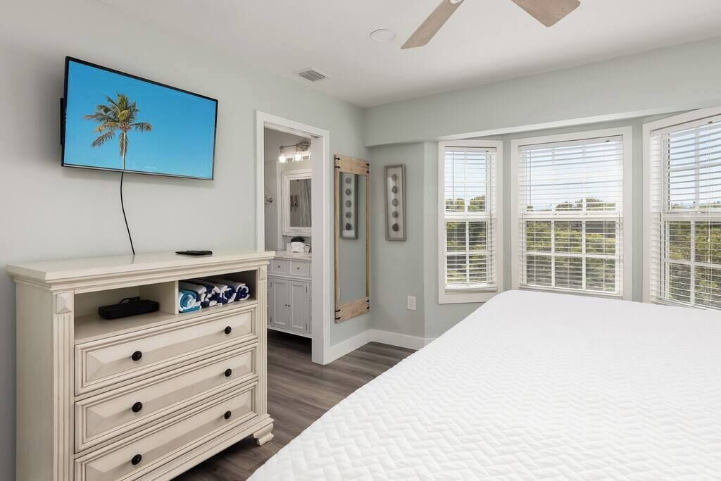 A bedroom with a bed, a dresser, a television, and a window with blinds.