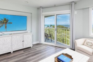 A room with a large sliding glass door leading to a balcony with a view of the ocean and greenery.
