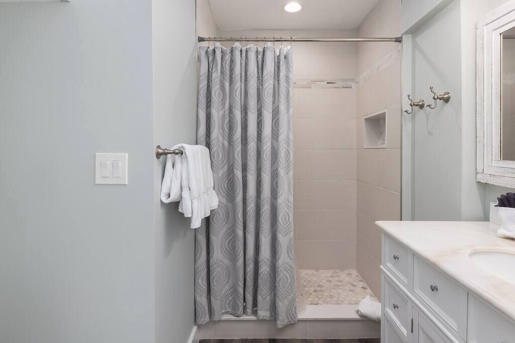 A bathroom with a shower, a towel rack with towels, a vanity with a mirror, and a light fixture on the ceiling.